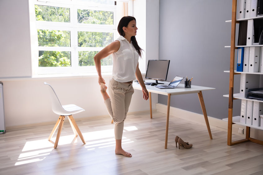 young business woman standing up and stretching in front of desk